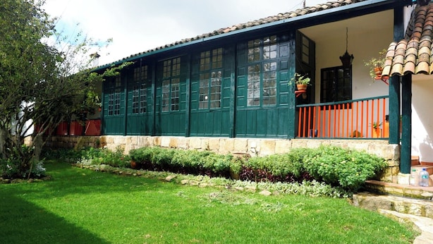 A two-story building with green-painted exterior walls, a tiled roof, and a small porch with orange railings. - Hacienda La Armenia - Cottage Hotel (Sopó)