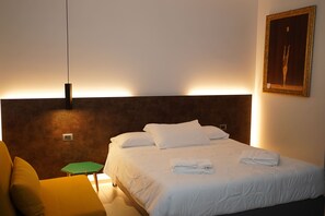 A hotel room with a bed, a bedside table, a chair, and a painting on the wall. - Tenuta San Marco (Noto)