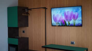Moderni huone, jossa on puupanelointi yhdellä seinällä, seinälle asennettu televisio, jossa näkyy kukkia, vihreä penkki ja naulakko.