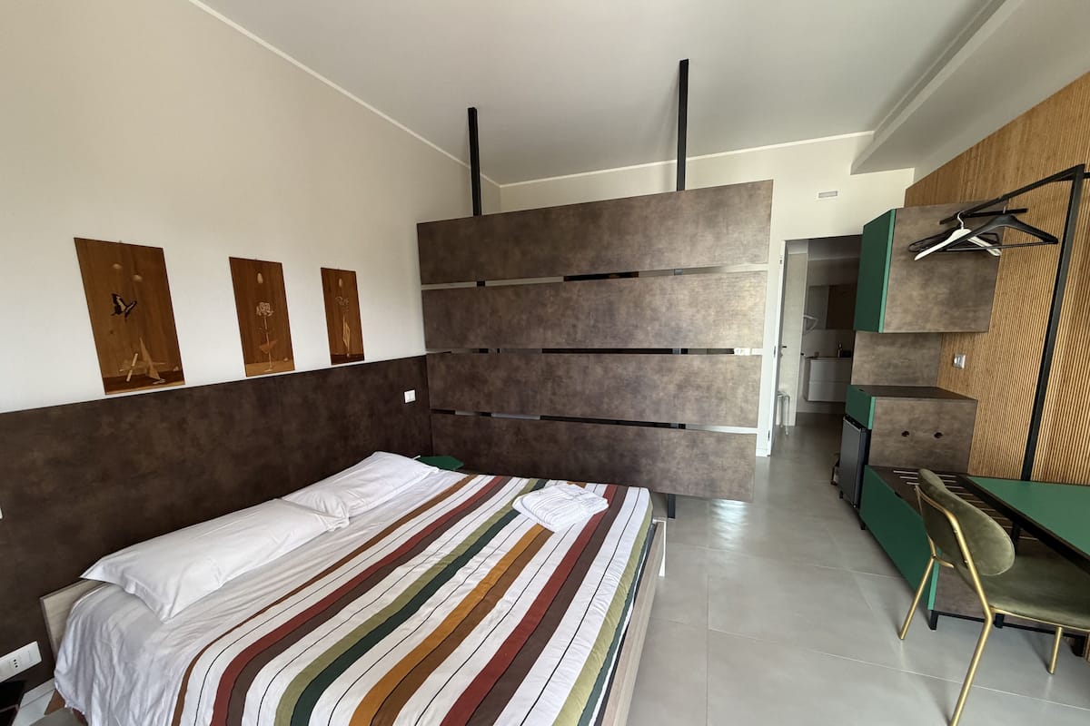A modern bedroom with a large bed, a desk, and a wardrobe.