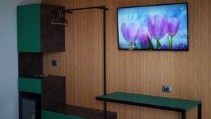 Ein modernes Zimmer mit einer Wandpaneele aus Holz, einem montierten Fernseher, der Blumen zeigt, einer grünen Bank und einem Kleiderständer.