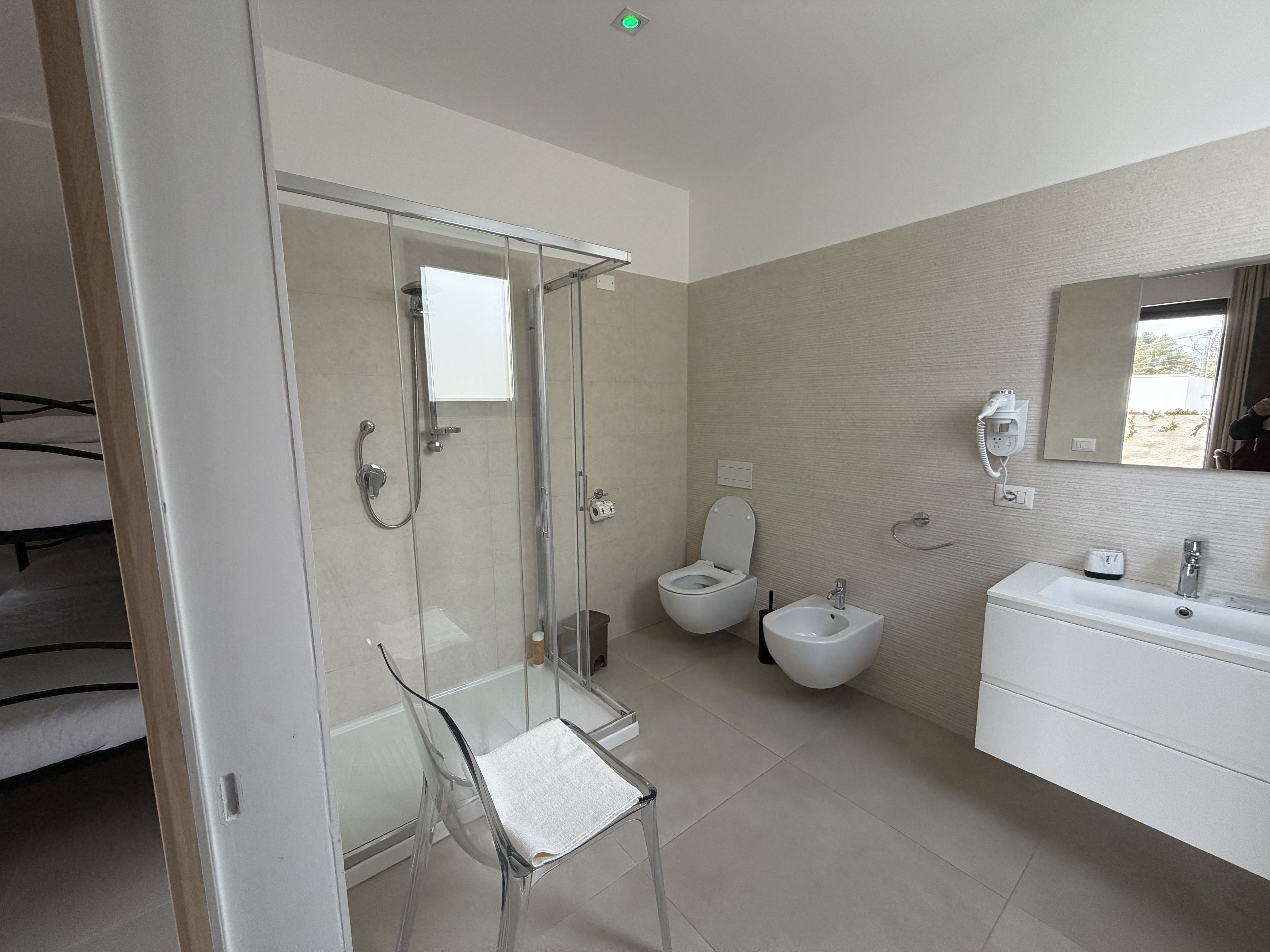 Uma casa de banho moderna com cabine de duche em vidro, sanita, bidé e lavatório branco com espelho em cima.