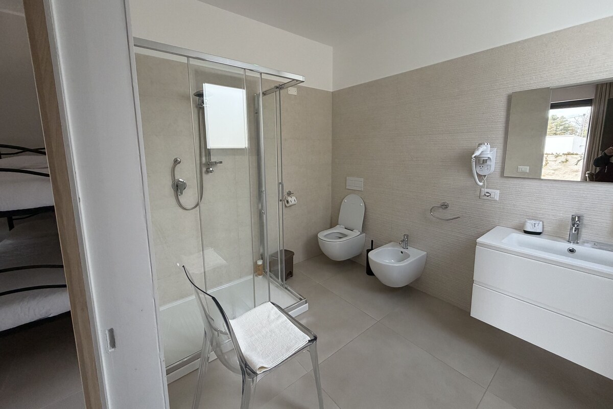 Un baño moderno con cabina de ducha de vidrio, inodoro, bidé y lavabo blanco con espejo arriba.
