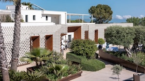 A modern building with a white facade, multiple balconies, and a landscaped garden with palm trees and shrubs. - Tenuta San Marco (Noto)
