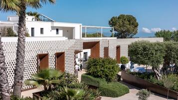 A modern building with a white facade, multiple balconies, and a landscaped garden with palm trees and shrubs.