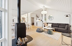 Un salon moderne avec une cheminée, un canapé, un coin repas et une cuisine en arrière-plan.