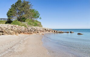 A beach with a rocky shoreline, clear water, and a building with a staircase leading up to it. - 3 bedroom stunning home in Martofte (Martofte)