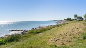 Een kustlandschap met een heldere lucht, een zandstrand en een graspaadje dat naar een rotsachtige kustlijn leidt.