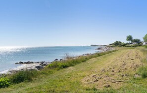 A coastal landscape with a clear sky, a sandy beach, and a grassy path leading to a rocky shoreline. - 3 bedroom stunning home in Martofte (Martofte)