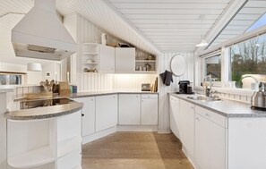 A modern kitchen with white cabinetry, granite countertops, and a large window providing natural light. - 3 bedroom stunning home in Martofte (Martofte)