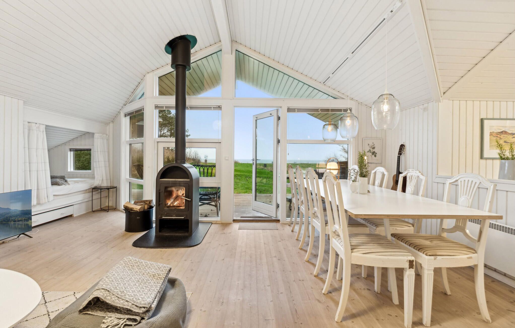 A spacious room with a large wooden table, white chairs, a fireplace, and a view of the outdoors.