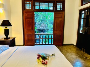 A hotel room with a bed, a nightstand with a lamp, and a window with wooden shutters. - Colonial Retreat Villa (Thalawatugoda)