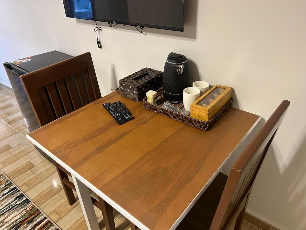 A wooden dining table with a remote control, a coffee maker, and a tray with cups and a box.