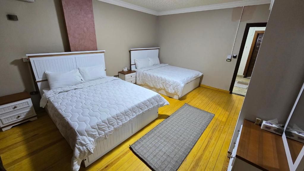 Un dormitorio con dos camas, suelo de madera y alfombra gris.
