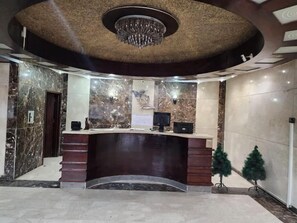 A reception area with a marble wall, a reception desk, a chandelier, and a small Christmas tree. - Skyline Luxury Suites 5 Mins From Cairo Airport (Cairo)