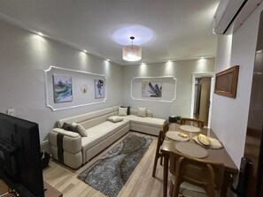A modern living room with a sectional sofa, a dining table with chairs, and artwork on the walls. - Skyline Luxury Suites 5 Mins From Cairo Airport (Cairo)