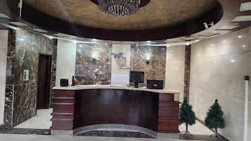 Zona de recepción con pared de mármol, mostrador de recepción, candelabro y un pequeño árbol de Navidad.