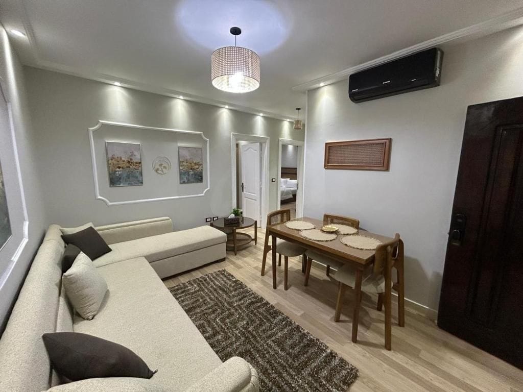 A living room with a sofa, a dining table with chairs, a rug, and wall-mounted artwork.