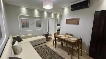 A living room with a sofa, a dining table with chairs, a rug, and wall-mounted artwork.