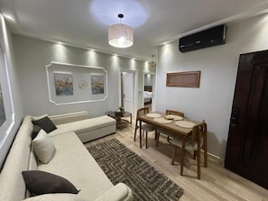 Een woonkamer met een bank, een eettafel met stoelen, een vloerkleed en kunst aan de muur.