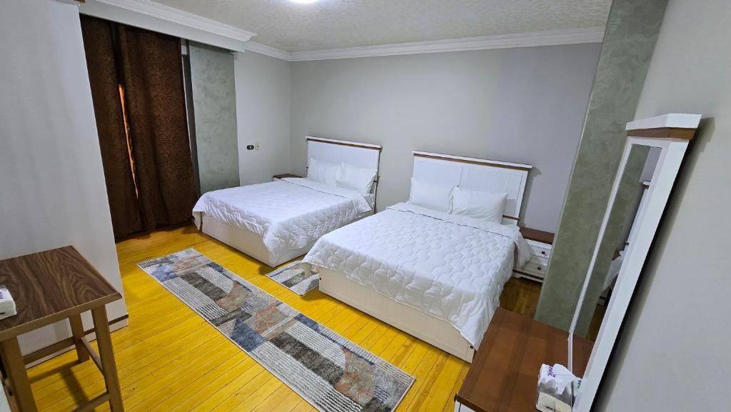 A room with two beds, a wooden floor, a small table, and a mirror.