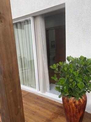 Piso de madeira, um vaso de planta e uma janela com cortinas.