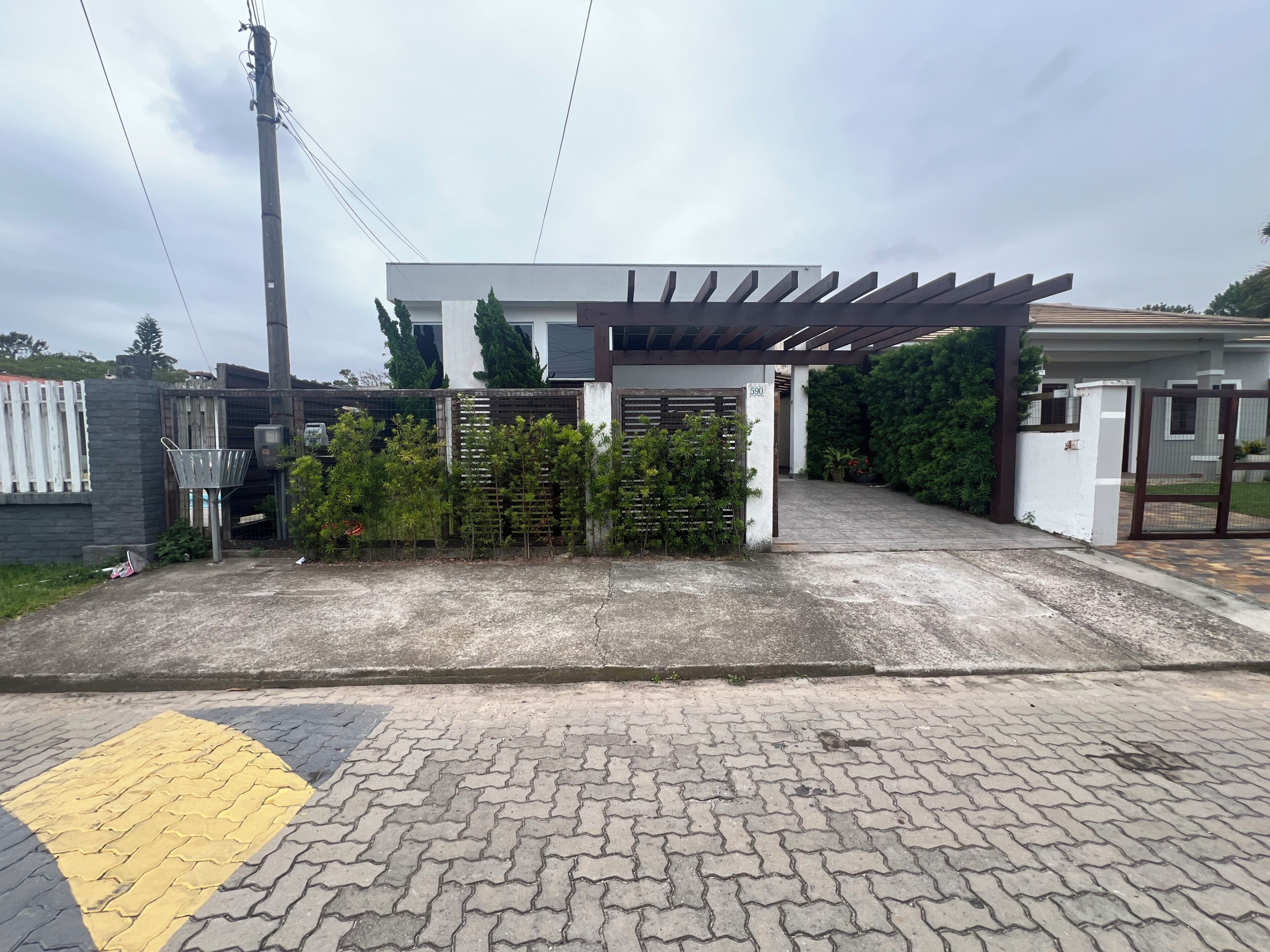 Uma entrada com portão, uma passarela coberta, um aro de basquete e um caminho de acesso pavimentado.