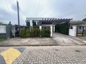 Uma entrada com portão, uma passarela coberta, um aro de basquete e um caminho de acesso pavimentado.