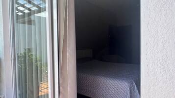Um quarto com uma cama, uma janela com cortinas e piso de madeira.