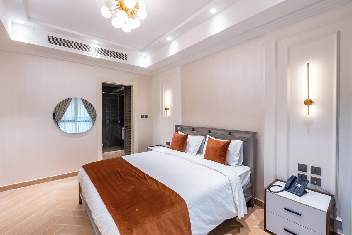 A modern hotel room with a large bed, bedside tables, a mirror, and a phone on the nightstand.