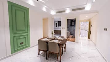 Uma sala de jantar com piso de mármore, uma porta verde e uma cozinha moderna ao fundo.