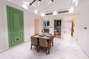 A dining area with a marble floor, a green door, and a modern kitchen in the background.