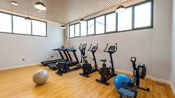 Un gimnasio con equipo de ejercicio, una pelota grande y ventanas amplias.