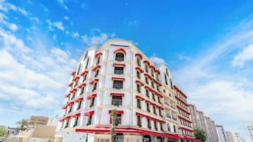 A multi-story hotel with a white facade, red awnings, and balconies with plants.
