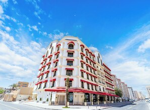 A multi-story hotel with a white facade, red awnings, and balconies with plants.