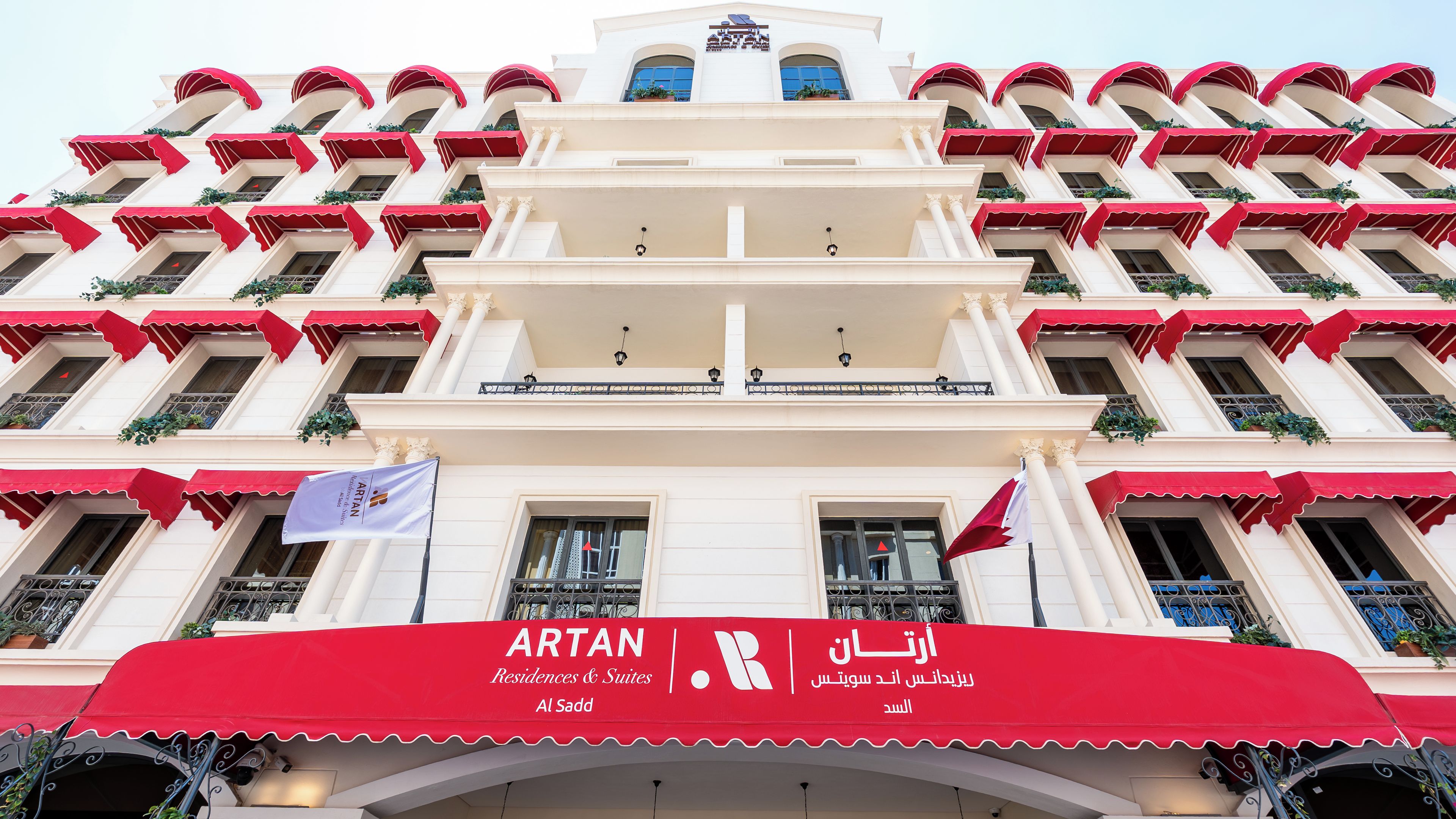 Un edificio de varios pisos con un toldo rojo que muestra 'ARTAN Residences & Suites' y texto en árabe.