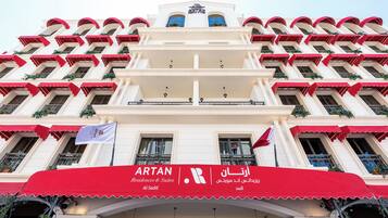 Un edificio de varios pisos con un toldo rojo que muestra 'ARTAN Residences & Suites' y texto en árabe.