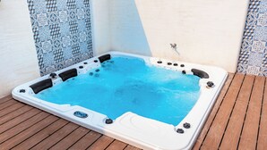 Un jacuzzi en una terraza de madera con una pared de azulejos al fondo.