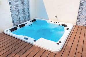 Un bain à remous sur une terrasse en bois, avec un mur carrelé en arrière-plan.