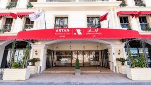 A hotel entrance with a red awning, a flag, and a sign in multiple languages. - Artan Residence & Suites (Doha)