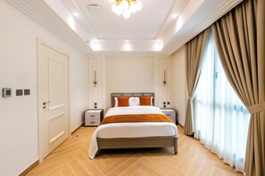 Una habitación de hotel con cama, mesitas de noche, armario y un ventanal con cortinas.
