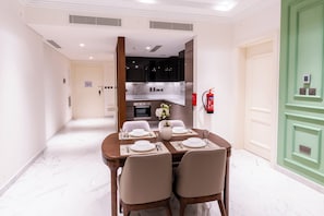 Un comedor con una mesa preparada para cuatro, una cocina al fondo y una puerta verde a la derecha.