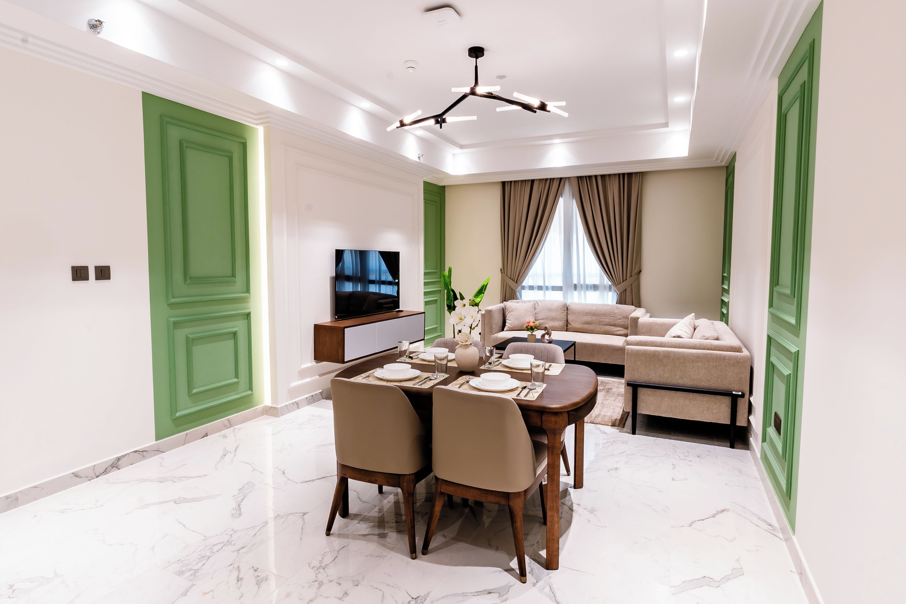 Una sala moderna con comedor, puertas verdes, televisor de pantalla plana y un conjunto de sofás.