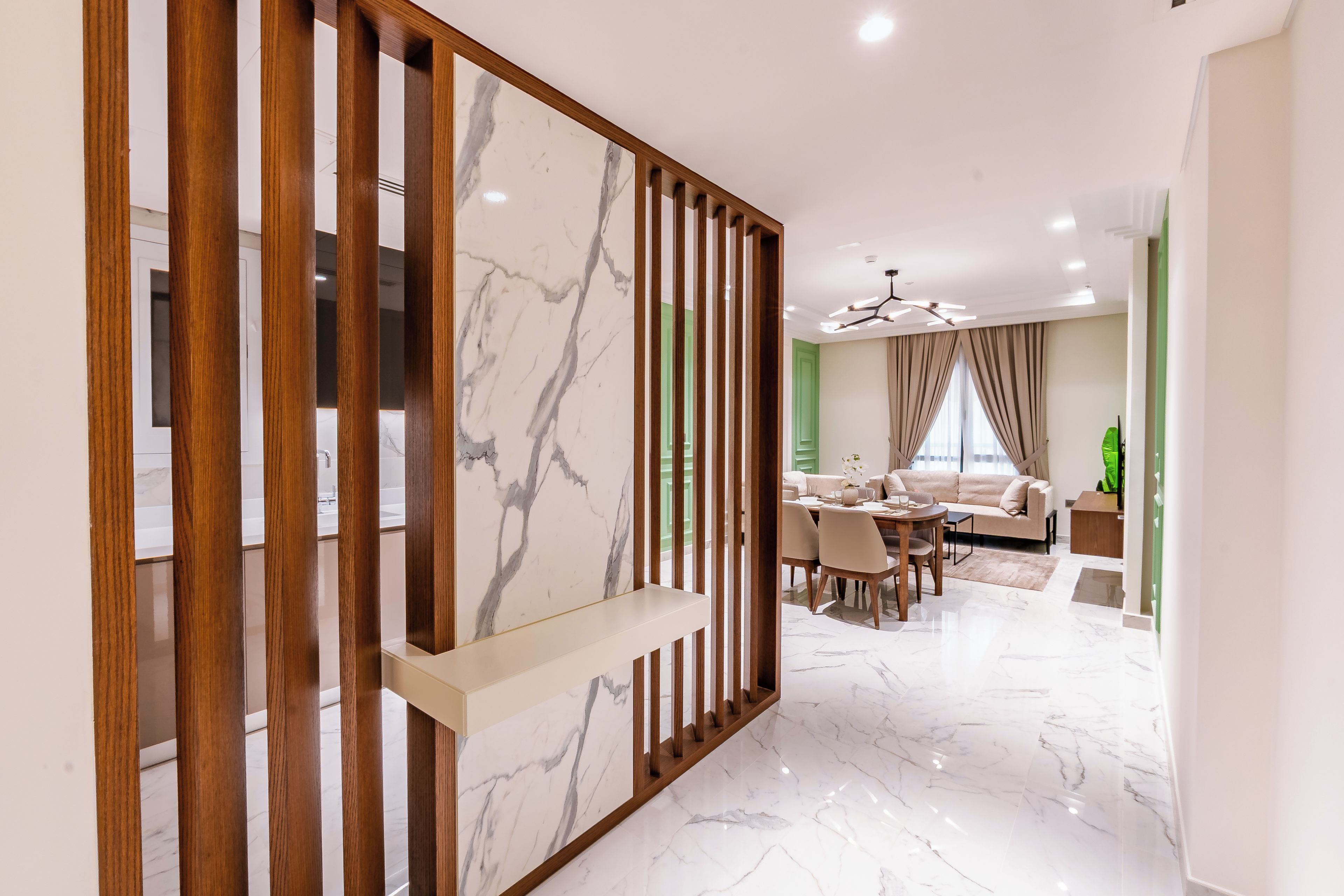 Un interior moderno con piso de mármol, un área de comedor con pared de acento verde y una sala de estar con sofá y planta verde.