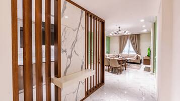 Un interior moderno con piso de mármol, un área de comedor con pared de acento verde y una sala de estar con sofá y planta verde.