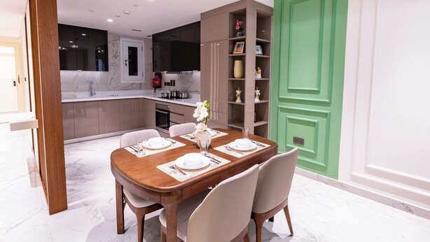 A dining area with a marble floor, a wooden table set for four, and a green door in the background. - Artan Residence & Suites (Doha)