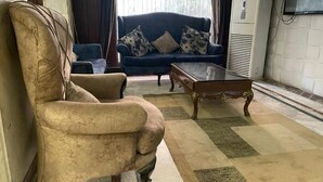 A living room with a beige armchair, a blue sofa with patterned cushions, and a wooden coffee table. - Al-manar Hotel (Giza)