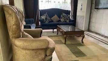 Una sala de estar con un sillón color beige, un sofá azul con cojines estampados y una mesa de centro de madera.