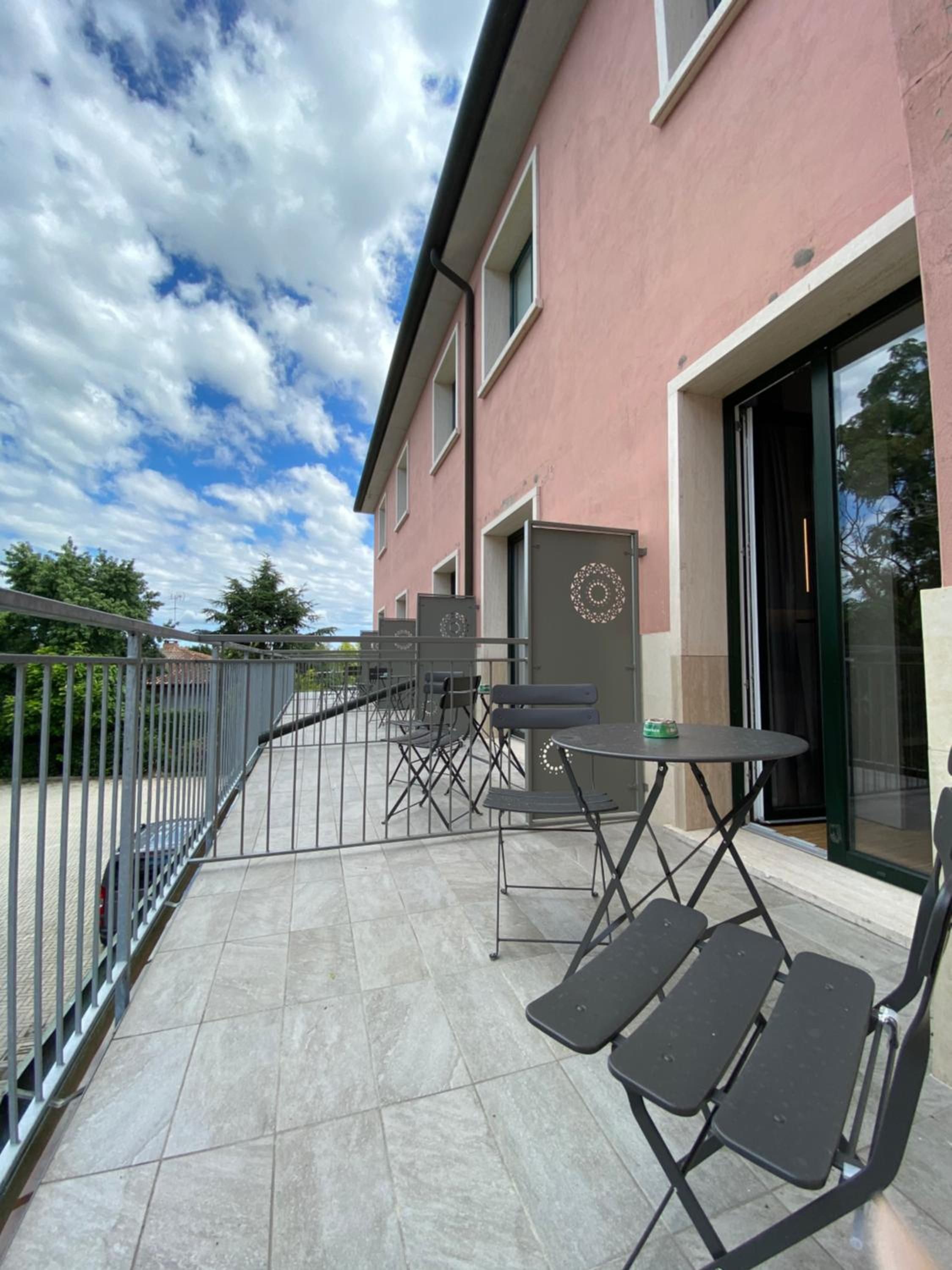 A balcony with outdoor seating, a building with a pink facade, and a clear sky.