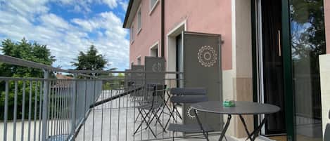 A balcony with outdoor seating, a building with a pink facade, and a clear sky.